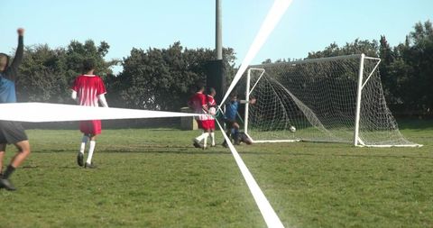 Youth goalkeeper diving to save goal as teammates celebrate on grassy soccer field, action