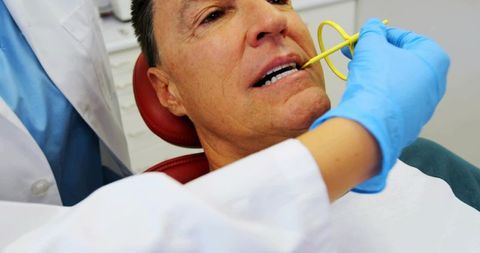 Reclining man receiving dental exam with yellow suction and blue-gloved dentist