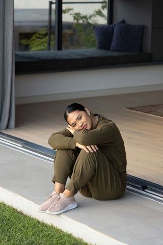 Asian woman sitting curled on patio threshold wearing olive loungewear relaxing at home