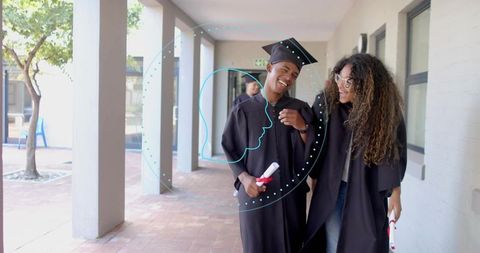 Graduates celebrating together walking campus corridor wearing gowns and holding diplomas