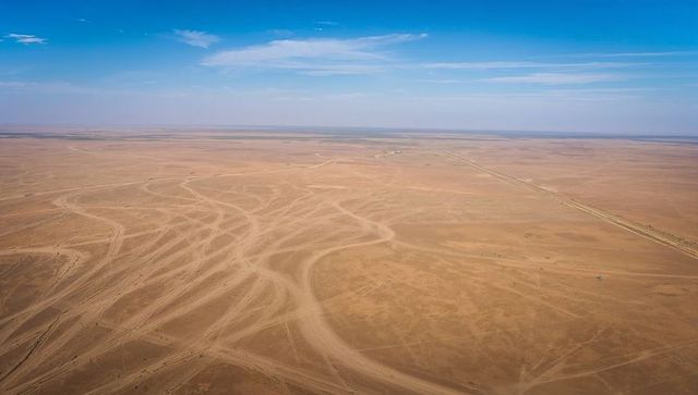 Aerial vista of vast desert plain showing winding tire tracks and unpaved road to horizon