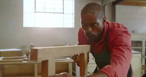 Focused carpenter adjusting wooden frame on workbench in bright workshop