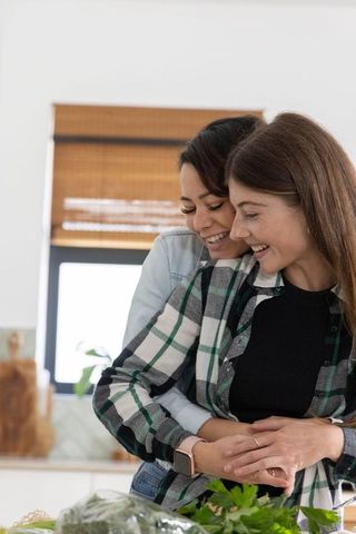 Couple hugging while preparing fresh salad in bright home kitchen