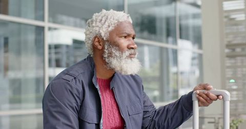 Senior African American traveler waiting at airport terminal looking thoughtful holding suitcase