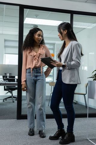 Diverse female coworkers discussing project at modern glass-partitioned office