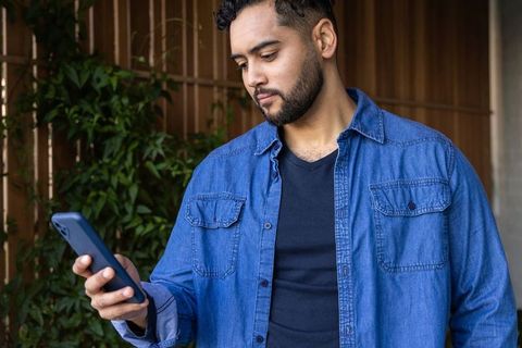Man checking smartphone on shaded patio wearing denim shirt and casual black tee