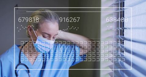 Tired nurse standing by window rubbing neck in blue scrubs wearing mask with hud overlay