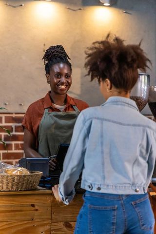Friendly african american barista serving customer at cozy cafe counter with pastries