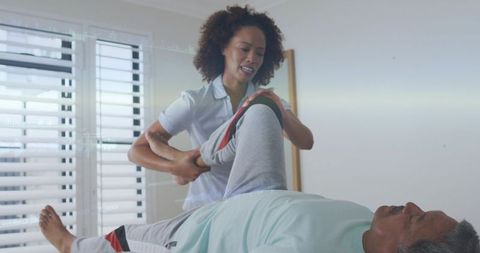 Female therapist assisting senior man with knee stretch on treatment table for mobility