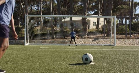 Youth players taking penalty kick with goalkeeper guarding goal on sunny artificial turf