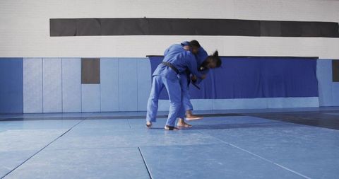 Martial artists practicing throw techniques in gym with blue mat