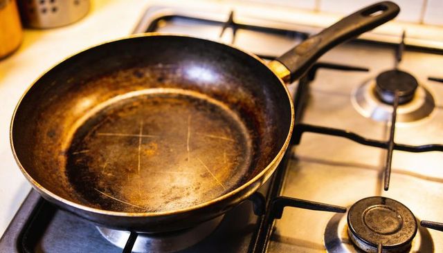 Worn frying pan resting on gas stove showing seasoning and scratches