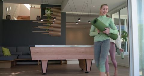 Women carrying yoga mats through modern minimalist recreation room with pool table