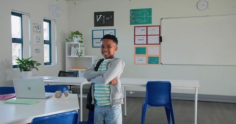 Confident African Student Standing with Arms Crossed in Bright Classroom with Laptop