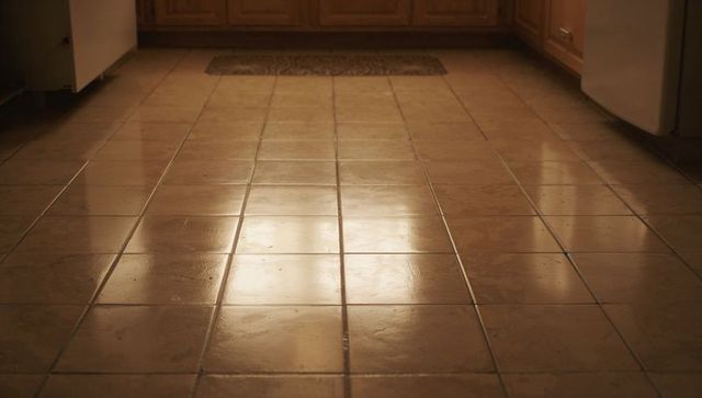 Glossy beige ceramic kitchen floor reflecting warm light with visible grout lines and mat