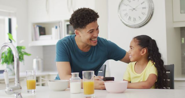 Happy biracial father and daughter eating breakfast and using smartphone together. domestic lifestyle, spending free time at home.