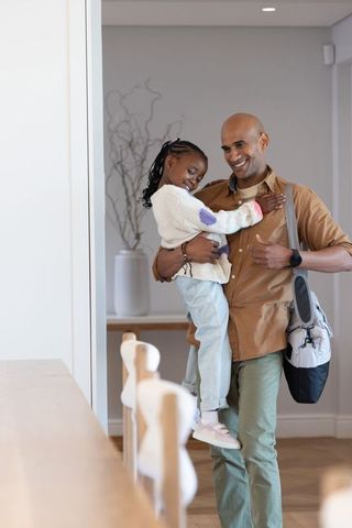Father carrying smiling african american daughter in modern hallway, family bonding