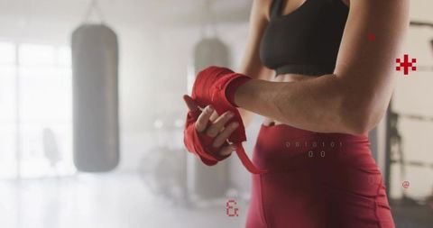 Female boxer wrapping hands with red wraps preparing for workout in bright boxing studio