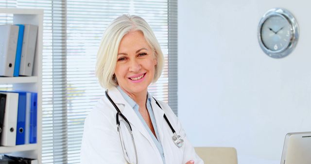 Senior female doctor smiling confidently in her office, wearing a white coat and a stethoscope. Ideal for healthcare, medical services, wellness programs, clinics, and hospital-related promotions. Useful for articles on healthcare professionals, medical advice, and patient care.