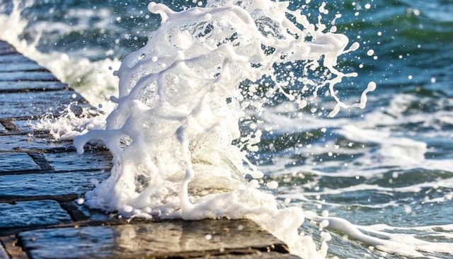 Crashing foam wave hitting wet stone jetty sending dramatic sea spray and reflections