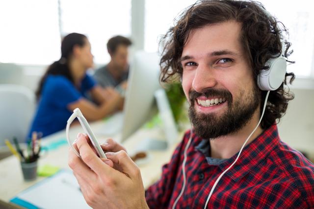 Male graphic designer listening music from mobile phone in office