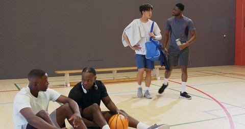 Young men resting after basketball practice on indoor court carrying bag and water bottle