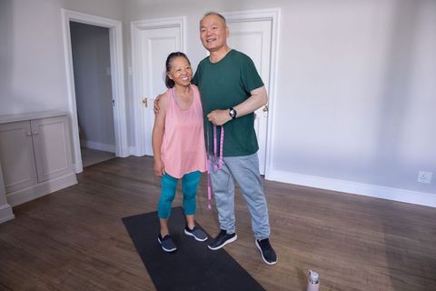 Senior asian couple exercising together at home holding pink measuring tape