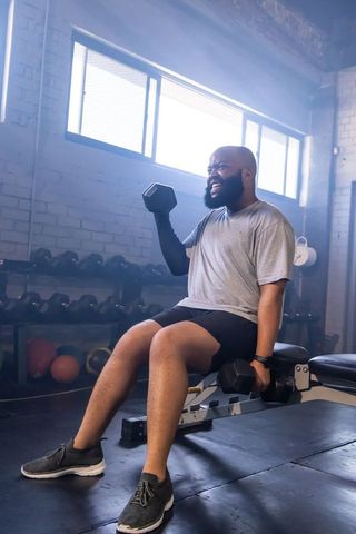 African american man lifting dumbbells on bench in industrial gym strength training