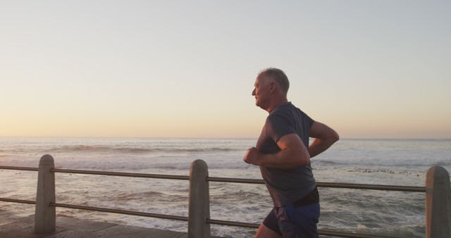 Senior man jogging along the oceanfront during sunset. Ideal for articles or ads related to fitness, outdoor activities, active aging, or promoting healthy lifestyles. Perfect for use in health campaigns, exercise programs, fitness blogs, and senior wellness services.
