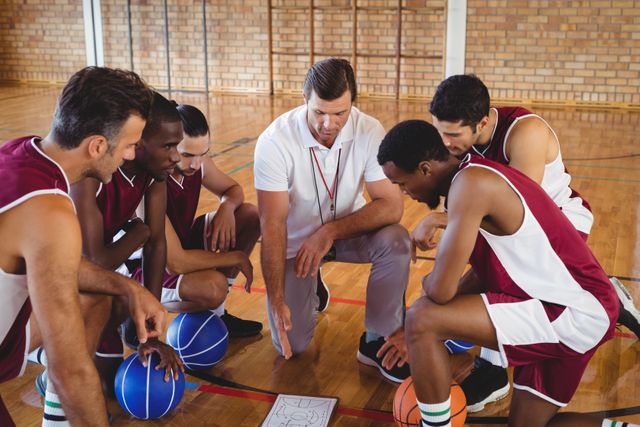 Coach discussing strategy with basketball players on indoor court. Ideal for sports training, teamwork, coaching, and athletic development themes.