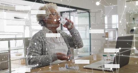 Senior woman taking medication at home table with laptop and telehealth interface