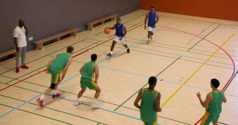 Basketball team practicing on indoor court with coach watching