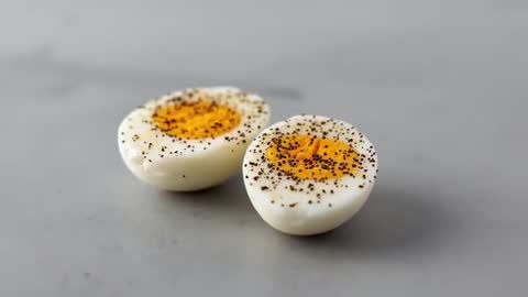 Macro Video Showing Two Hard-Boiled Egg Halves Sprinkled with Black Pepper on Gray Tabletop