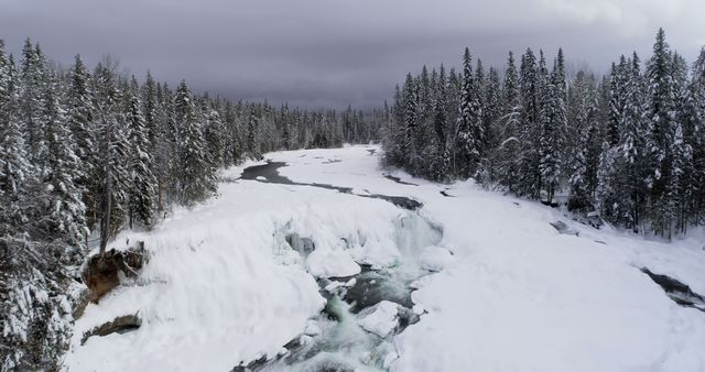 Snow-covered forest with a river flowing through the winter landscape. Evergreen trees stand tall, blanketed in snow, creating a serene and tranquil scene. Ideal for use in nature and winter-themed marketing materials, travel promotions, winter sports advertisements, and holiday season content.