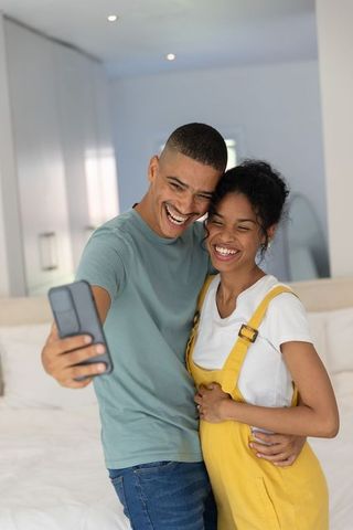 African american couple taking selfie while expecting baby, woman cradling belly