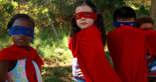 This image shows a diverse group of children dressed as superheroes with red capes and masks, playing in an outdoor setting. Their confident poses convey a sense of adventure and teamwork. This could be used for themes related to childhood fun, imaginative play, diversity, and friendship, ideal for promotional materials, educational content, or any context highlighting the joys of childhood.