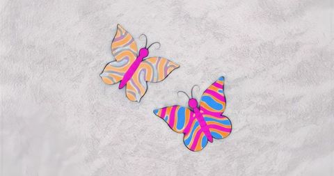 Vibrant striped butterfly cutouts lying on soft white textured fabric for craft decor