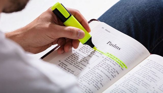 Man highlighting psalms in open bible on lap with yellow highlighter for devotional study