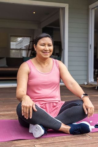 Mature woman practicing outdoor yoga on home deck in pink top and leggings for wellness