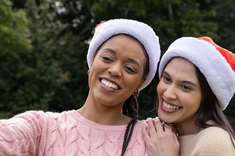 Smiling diverse women wearing santa hats and knit sweaters enjoying festive outdoor moment