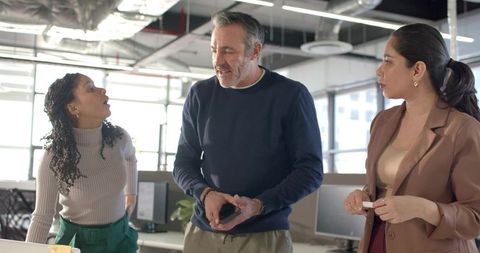 Diverse team brainstorming around workstation in modern open-plan office with smartphone
