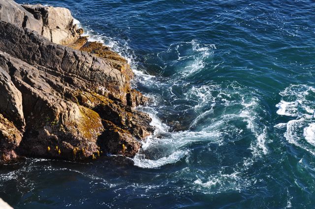 Waves crashing against rocky shoreline with clear blue water below. Natural coastline setting evokes feelings of power and tranquility. Perfect for use in travel promotions, nature documentaries, relaxation videos, and backgrounds for ocean-related content.