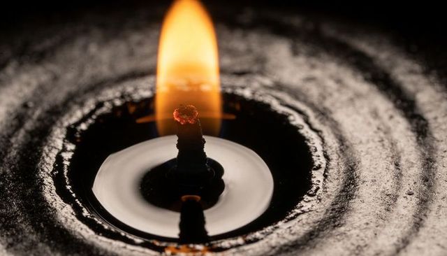Macro candle wick with tall flame and concentric melted wax reflection, moody ritual