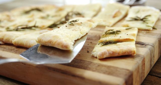 Freshly baked flatbread on a wooden cutting board garnished with rosemary, ready to be served. Ideal for food blogs, culinary websites, recipe books, and restaurant menus. The rustic setting emphasizes homemade, artisanal craftsmanship and natural ingredients.