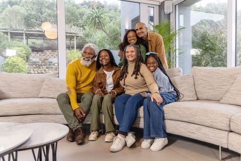 Smiling multigenerational african american family posing on sectional sofa in modern living room