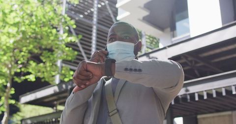Businessman using smartphone and smartwatch outdoors during pandemic