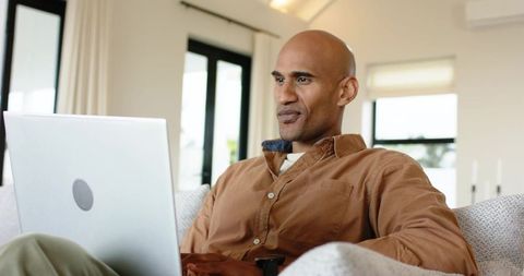Mature man working from home on laptop in bright minimalist living room