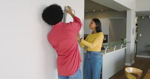Diverse couple hanging picture frame on wall in modern home