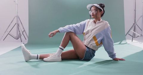 Asian model posing on mint-green backdrop in pastel colorblock jacket and denim shorts