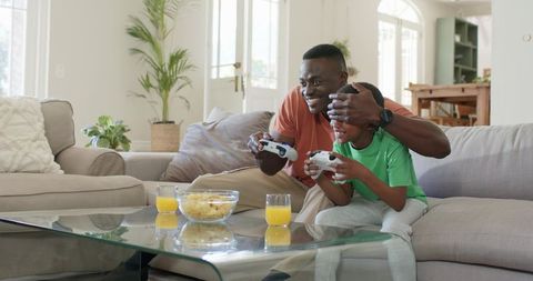African American Father and Son Playing Video Games on Sofa Sharing Joyful Bonding Moment